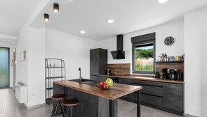 Una cocina moderna con una isla central, taburetes de bar, horno empotrado y ventana con vistas a zonas verdes.
