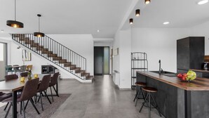 Una cocina moderna con una isla central, taburetes de bar y una escalera que lleva a otro nivel.