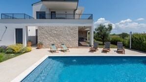 Una casa moderna de dos pisos con piscina, muro de piedra y zona de estar al aire libre.