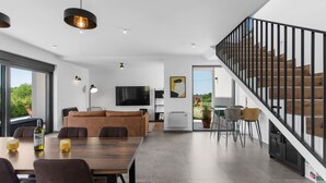 Un salón moderno con una mesa de comedor de madera, sofás y una escalera con barandillas negras.
