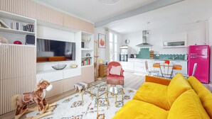 En moderne stue med et fjernsyn, bogreoler, en gyngehest og en farverig gul sofa.