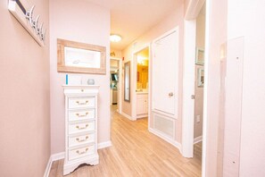Un pasillo con un aparador blanco, un cuadro enmarcado y una puerta que da a otra habitación.