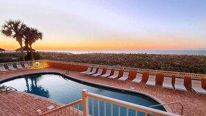Une piscine avec des chaises longues et une vue sur la plage au coucher du soleil.
