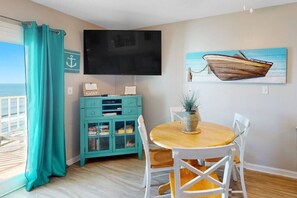 Una habitación con un armario color turquesa, una mesa de madera con sillas blancas, un televisor de pantalla plana y un cuadro de un barco.