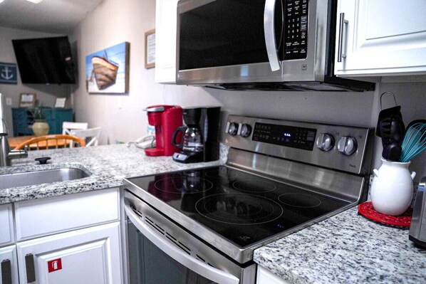 A modern kitchen with stainless steel appliances, a granite countertop, and white cabinetry.