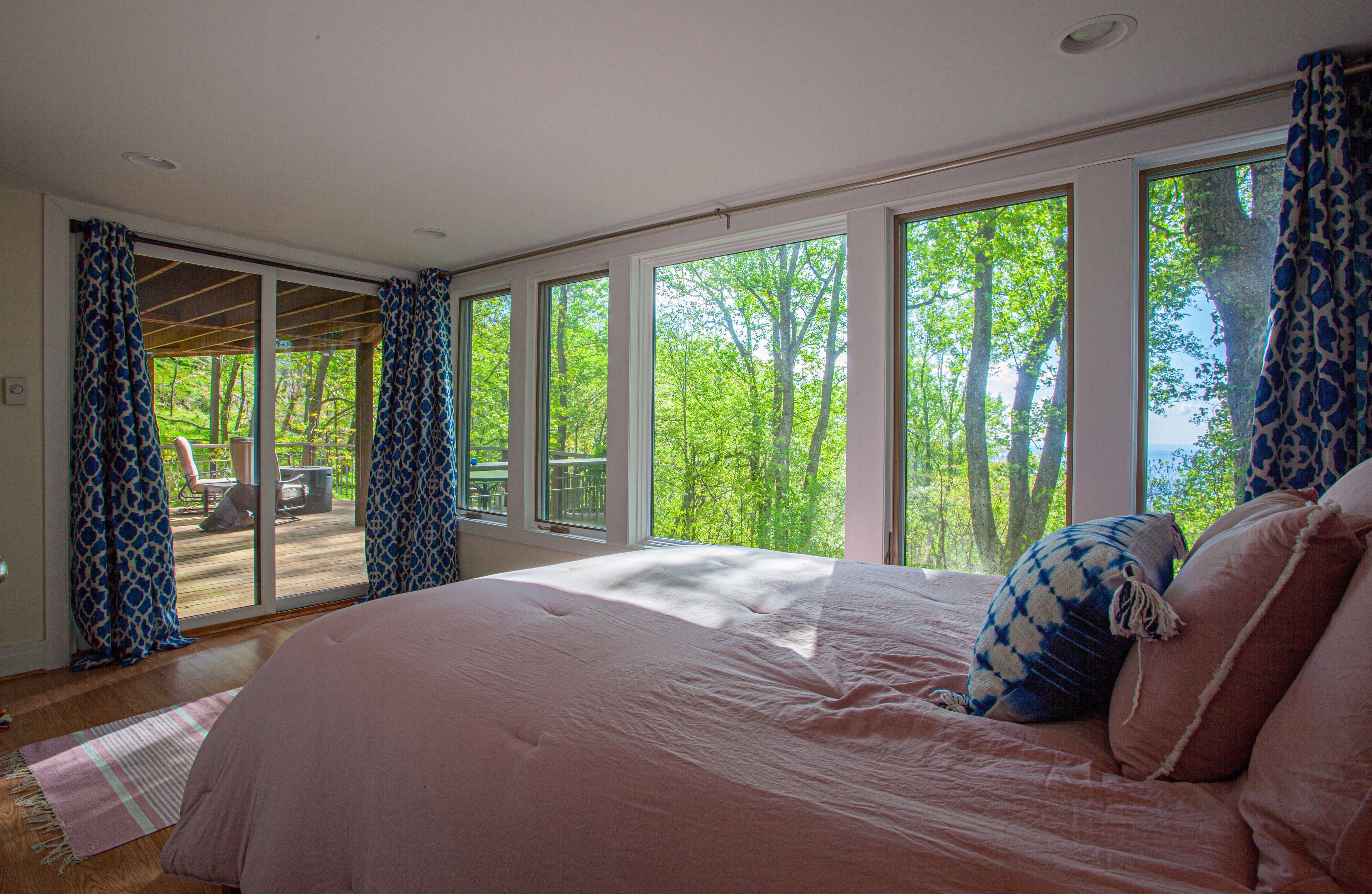 A bedroom with a large bed, multiple windows, and a view of trees.