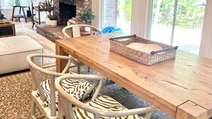 A cozy living room with a fireplace, a large window, and a dining area with zebra-striped chairs. - Katama Retreat W Pickle ball Court (Edgartown)