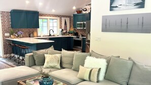 A modern living room with a sectional sofa, a coffee table, and a kitchen in the background. - Katama Retreat W Pickle ball Court (Edgartown)