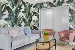 Un salon avec un canapé gris, une table basse en verre, un fauteuil rose et un grand meuble-miroir.