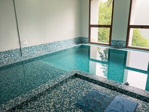 Una piscina con borde de azulejos y una ventana con vistas a la vegetación.