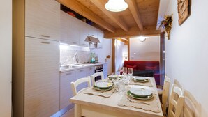 Une cuisine moderne avec des meubles blancs, une table à manger dressée pour quatre personnes et un canapé rouge en arrière-plan.