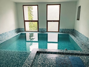 A swimming pool with a tiled edge and a view through two windows.
