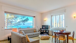 Una sala de estar con sofá, televisor, mesa de comedor y sillas, y vista al mar.