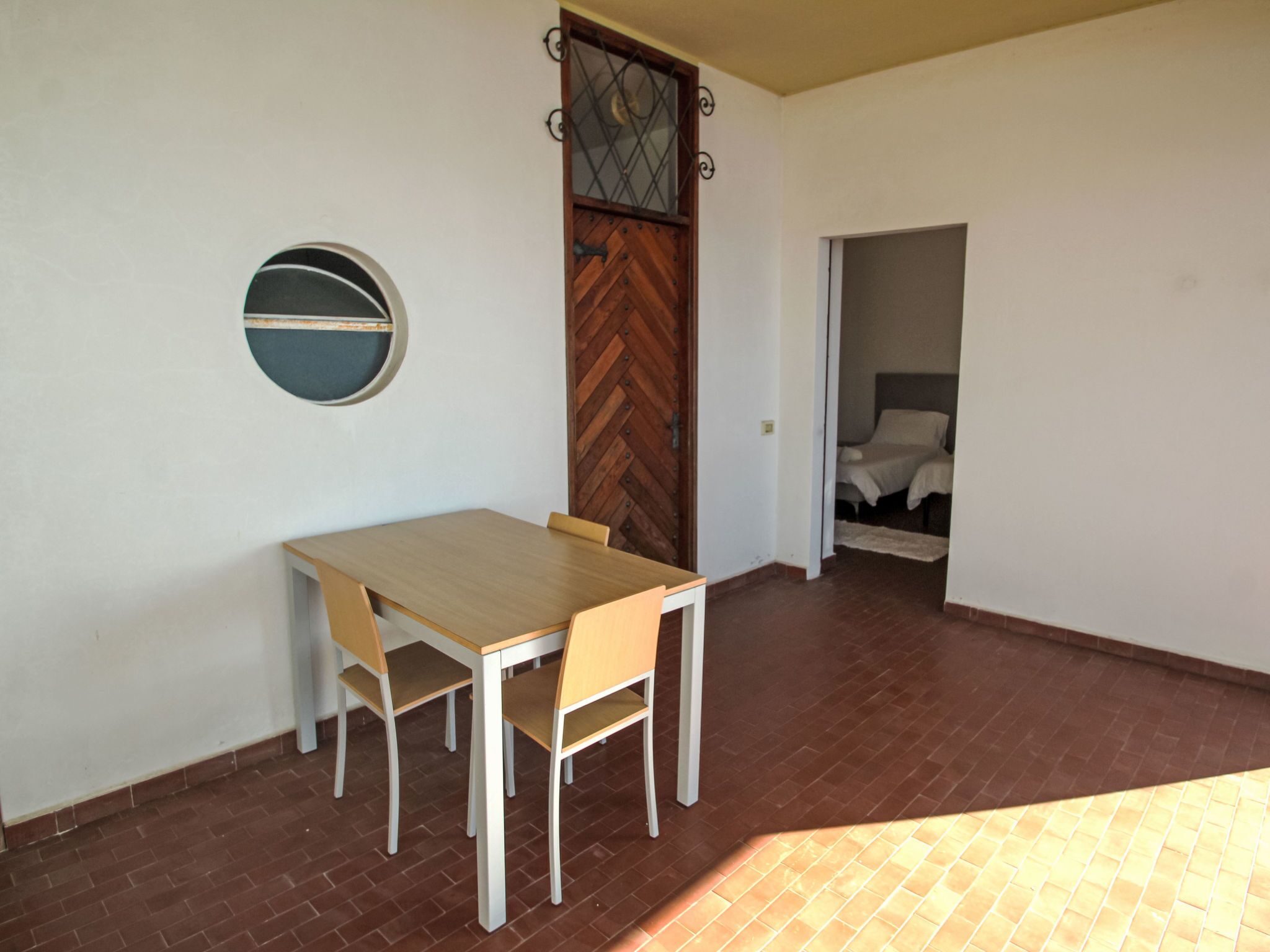 Un coin repas avec une table et des chaises en bois, une fenêtre ronde et une porte à motifs en chevrons.