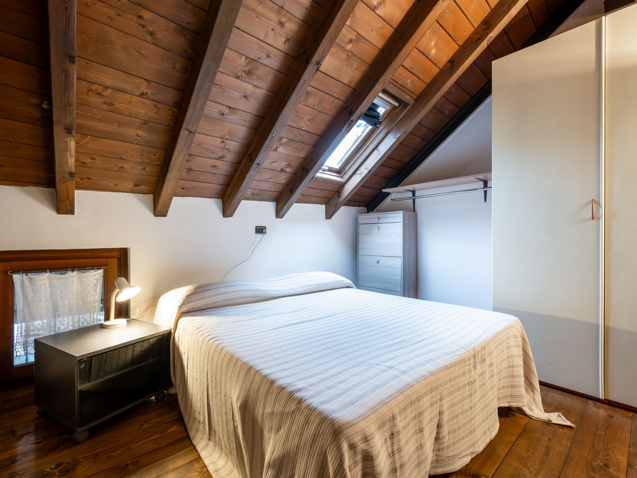 A bedroom with a bed, a nightstand, a wardrobe, and a skylight.