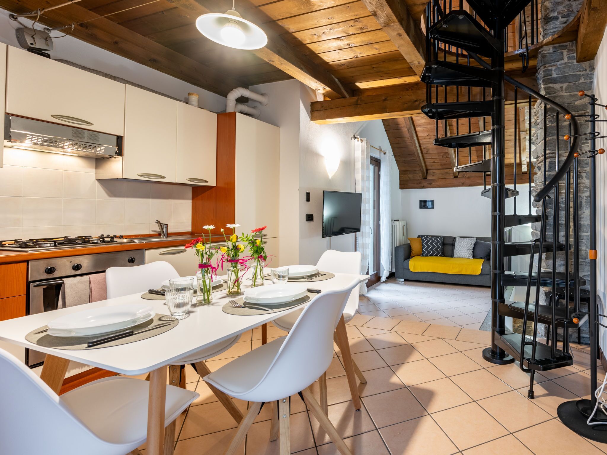 A modern kitchen with white cabinets, a dining table set for four, and a spiral staircase.