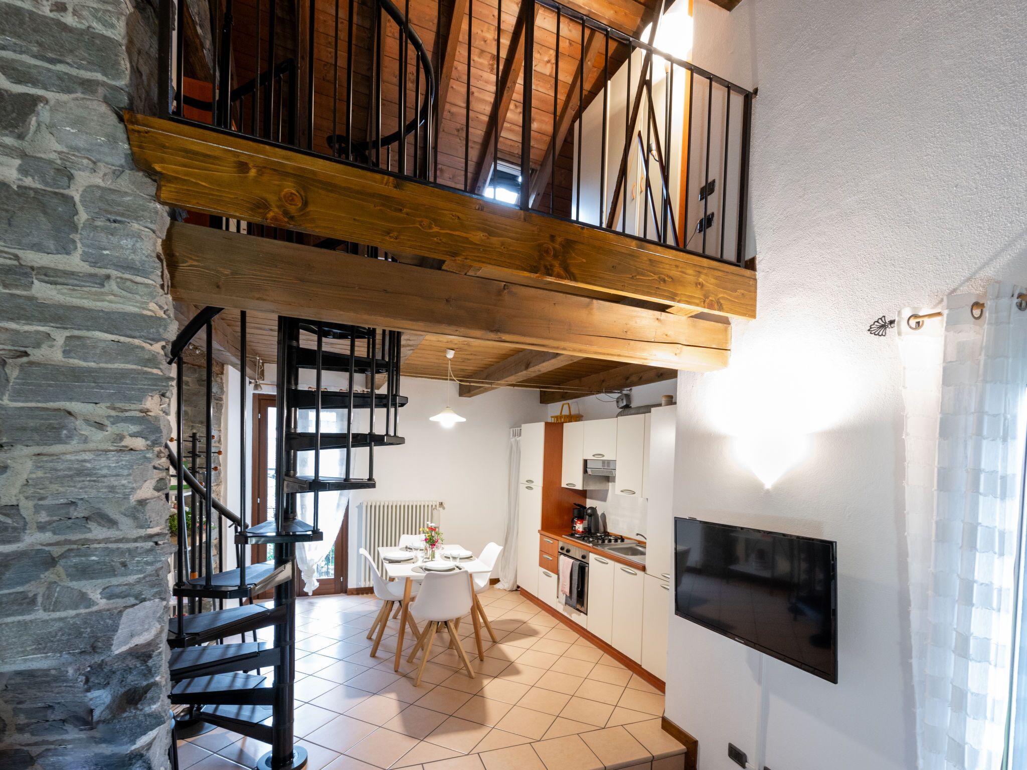 A spacious kitchen with a dining area, a staircase leading to an upper level, and a stone wall.