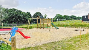 Ein Spielplatz mit einer Holzspielanlage, einer roten Rutsche und einer grünen Rutsche.