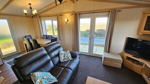 A cozy living room with a leather sofa, a dining table, and a TV on a wooden stand. - Penmor -  a holiday home that sleeps 6 guests  in 3 bedrooms (Bude)