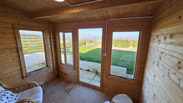 A wooden cabin with large windows offering views of a grassy field and distant hills. - Penmor -  a holiday home that sleeps 6 guests  in 3 bedrooms (Bude)