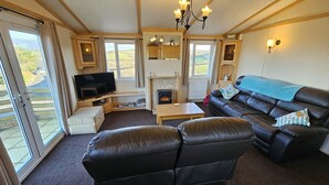 A cozy living room with a fireplace, leather sofa, and a television. - Penmor -  a holiday home that sleeps 6 guests  in 3 bedrooms (Bude)