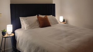 A neatly made bed with a dark headboard, two bedside lamps, and a small potted plant on a side table. - Stay and Relax at Beachfront Beauty (Whangaparāoa)