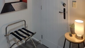 A white door with a handle, a wall-mounted towel rack, a small table with a lamp, and a potted plant. - Stay and Relax at Beachfront Beauty (Whangaparāoa)