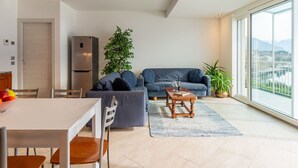 Een moderne woonkamer met een bank, een eettafel en stoelen. Er is een groot raam met uitzicht op een stad en bergen.