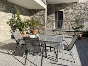 Une terrasse avec une table et des chaises, entourée de plantes en pot et d’un mur de pierre.
