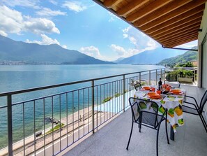 Un balcon avec une table dressée pour le dîner, donnant sur un lac et offrant une vue sur des montagnes en arrière-plan.