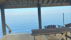 Une terrasse en bois offrant une vue sur l’eau, un espace salon couvert et une rambarde en métal.