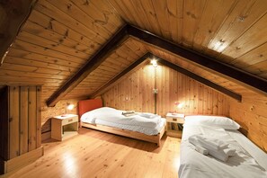 Una habitación de madera con techo inclinado, una cama con ropa de cama blanca y dos mesitas de noche con lámparas.