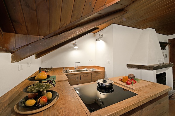 Una cocina con armarios de madera, una cocina por inducción negra y una exposición de frutas.