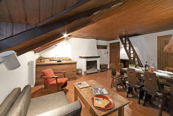 Een knus loft-appartement met houten plafond, een open haard, een eethoek en een keukentrap.