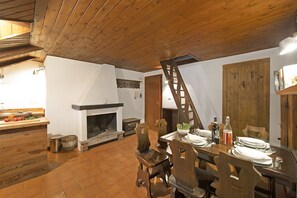 Un coin repas avec une table en bois dressée pour quatre personnes, une cheminée et un plafond en bois.