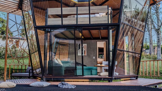 Una habitación moderna, con paredes de vidrio, que incluye una cama, zona de estar y vistas al exterior.