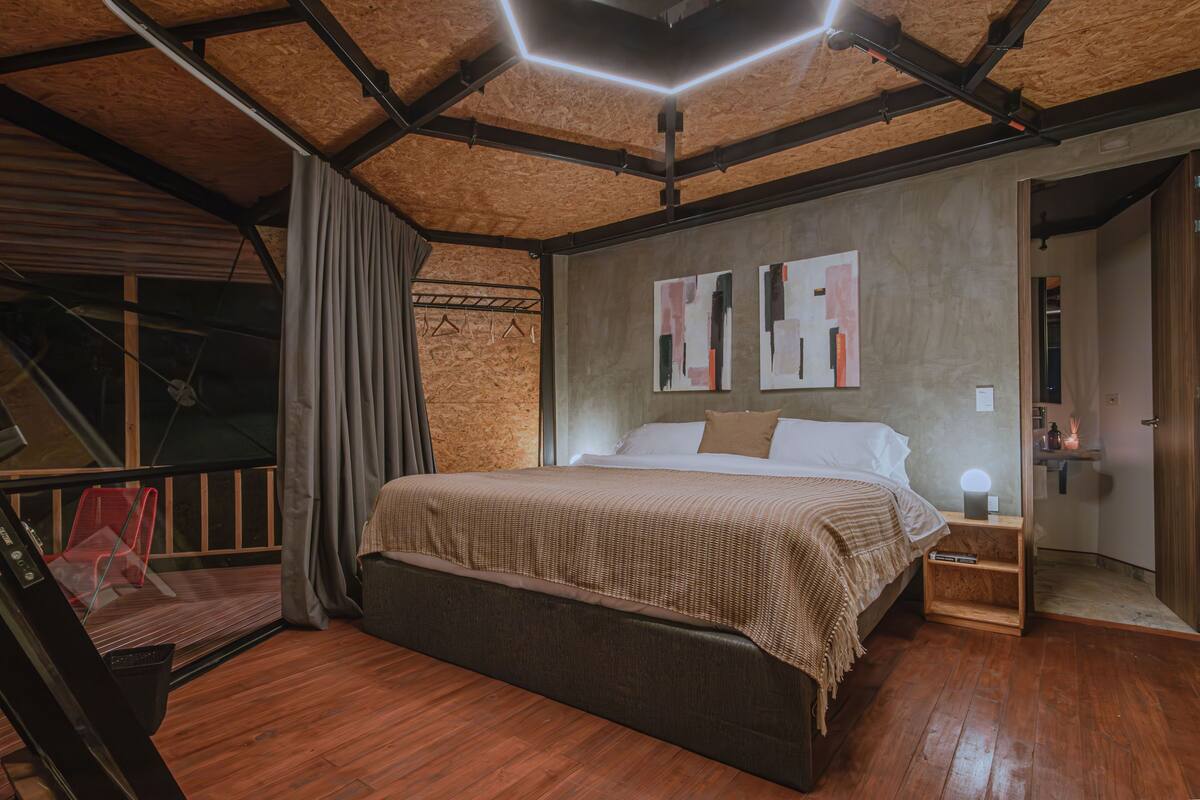 Un dormitorio moderno con una cama grande, suelo de madera y un balcón con una silla roja.