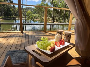 Eine Holzterrasse mit einem Tisch, der für ein Frühstück gedeckt ist, mit einer Fruchtschale und zwei Behältern mit Granola.