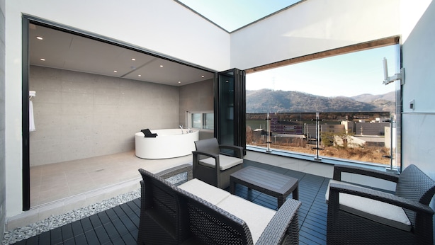 A modern balcony with a jacuzzi, wicker furniture, and a view of mountains.