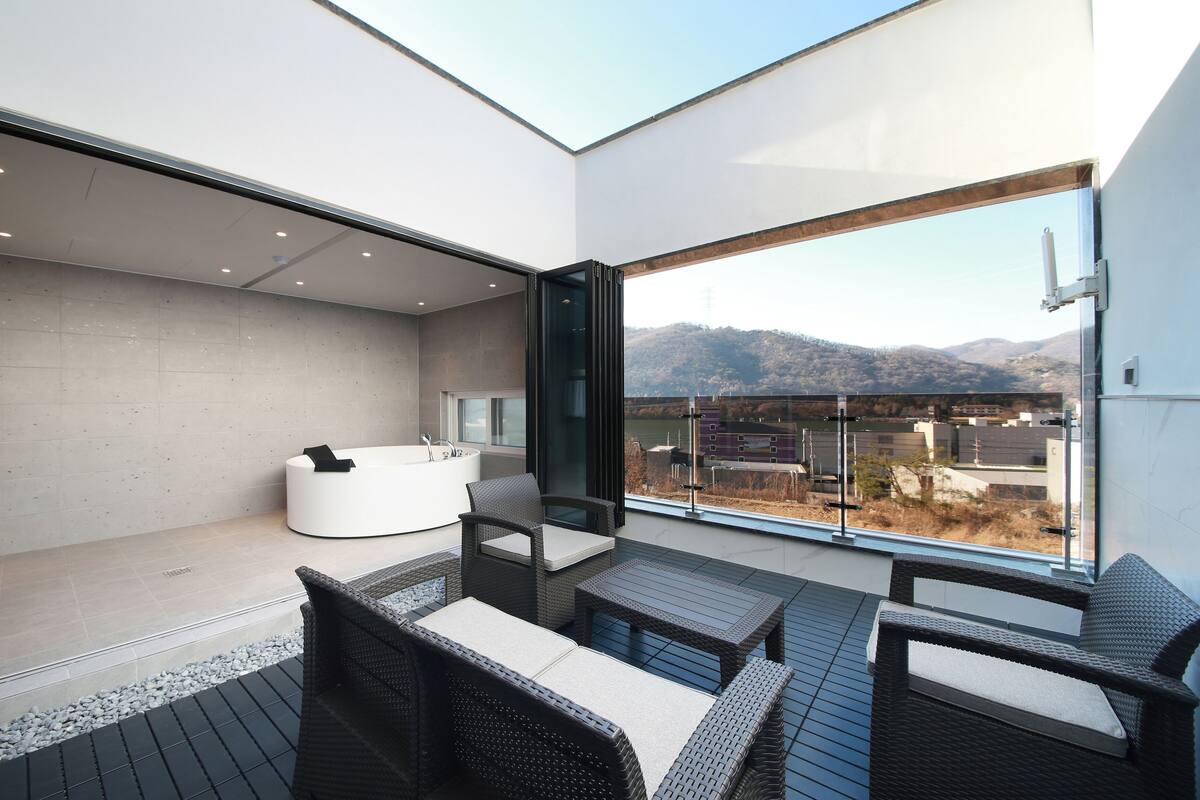 A modern balcony with a jacuzzi, wicker furniture, and a view of mountains.