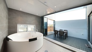 A modern bathroom with a large bathtub, a window, and a balcony with outdoor seating.