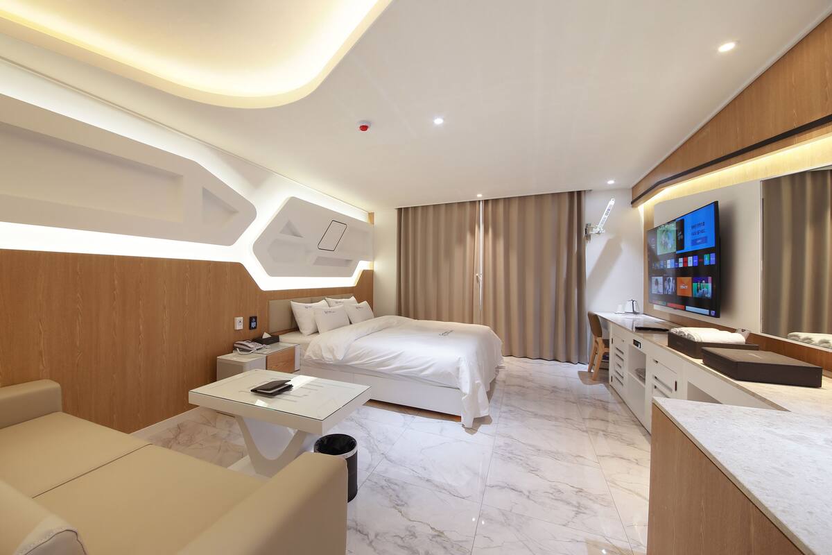 A modern hotel room with a bed, a desk, a chair, a TV, and a bathroom.