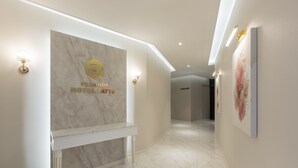 A modern hotel reception area with a marble wall, a reception desk, and a hallway leading to the rooms.