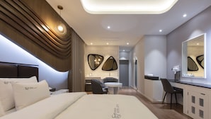 A modern hotel room with a large bed, a desk, and a chair. There is a small table and a mirror on the wall.