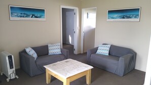 Ett rum med två grå soffor, ett soffbord i trä och två inramade tavlor med motiv av berglandskap.