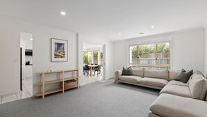 Ein geräumiges Wohnzimmer mit grauem Teppich, einem beigen Sofa und einem Holztischchen.