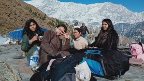 A group of people sitting on a stone ledge with a mountainous backdrop. - Triund Trek and Camping (Dharamshala)