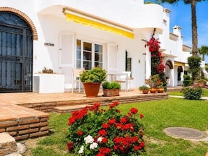 Un bâtiment blanc avec une porte noire, des plantes en pot et un petit espace patio.