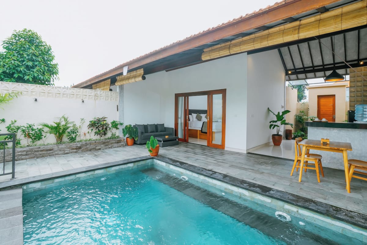 A pool area with a wooden deck, outdoor furniture, and potted plants.