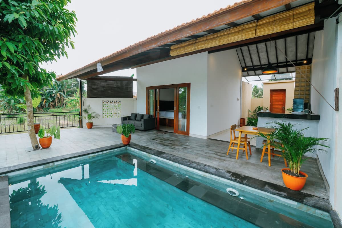 A swimming pool with a tiled deck, surrounded by potted plants and a wooden pergola.